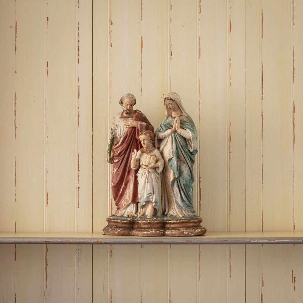 Statue of the Holy Family- Joseph, Mary, and Jesus- on a shelf against a wooden wall.