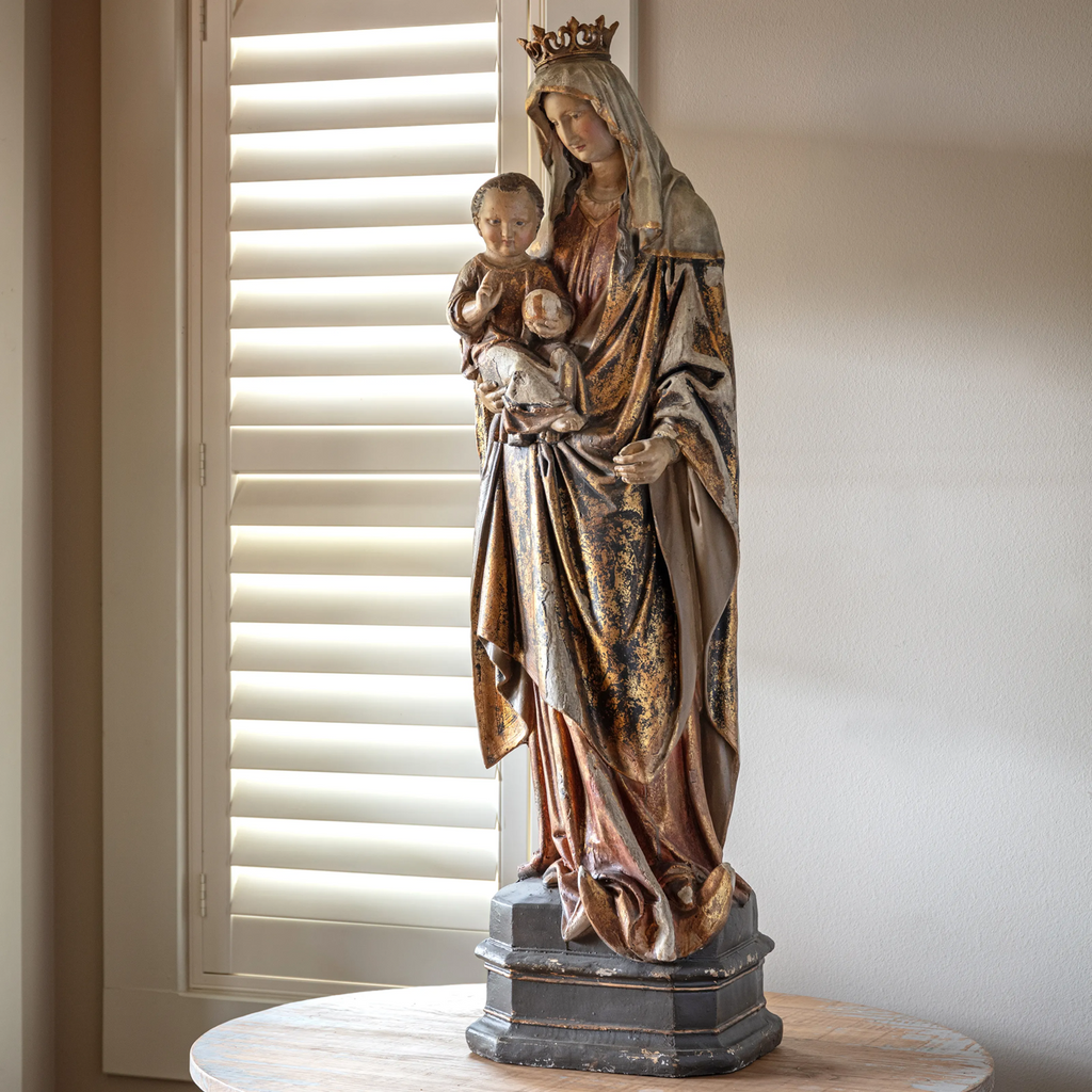 Statue of Madonna holding Baby Jesus on a table with a window in the background